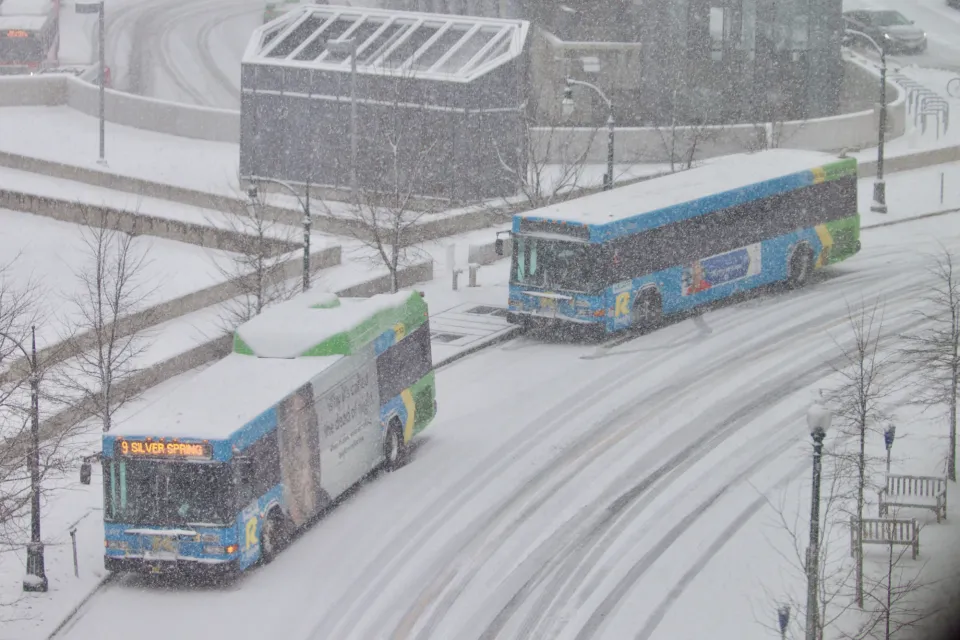 Two buses pull up to a station on a snowy day.